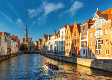 Auf einem Kanal in Bruegge faehrt ein Ausflugsboot. Die historischen Haeuser werden von der Sonne angestrahlt. | © Gettyimages.com/KavalenkavaVolha